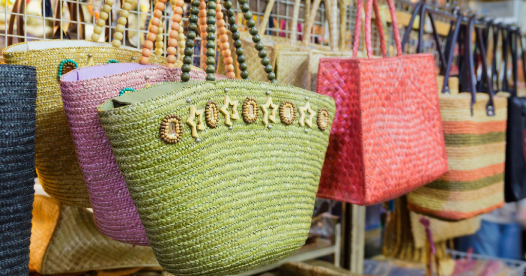 Colorful Straw Bags on display at a vibrant market. A variety of eye-catching designs and hues adorn the rack.