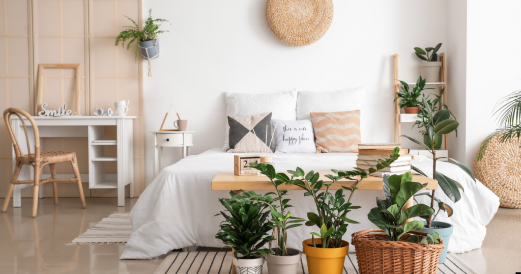 A bedroom with a bed, desk, chair, and potted plants. 