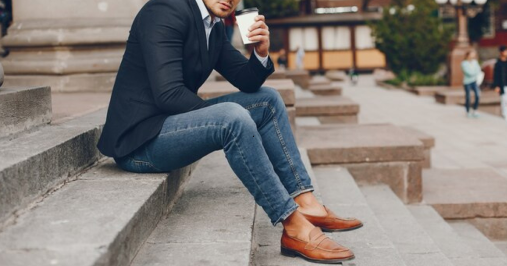 A man in a suit sitting on steps, holding a coffee cup, wearing Casual Brown Shoe