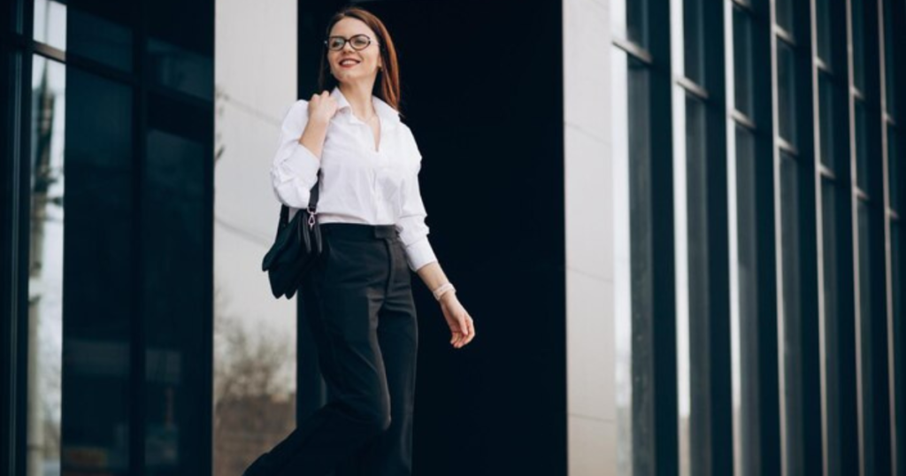 A stylish woman in a white shirt and black pants confidently striding forward.